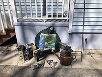 Photo showing lot contents including boxed solar lights, metal watering can, hanging baskets, garden hooks, and the packaged 6 ft pop-up garden trellis screen room.
