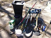 Overview of gardening lot including large planter, tools, watering can and trimmer.