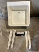 Top view of white laundry tub, four white legs laid out below, faucet still boxed