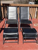 Pair of black leather chairs with chrome frames and matching stools shown on wooden deck under sunlight