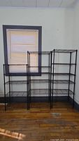 Full view of three metal wire shelving units in front of window, showing varying heights and wire shelf construction.