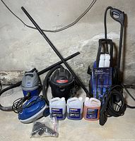 Full lot view showing ProSteam canister steamer, two shop vacuums (4 gal and 2.5 gal), Campbell Hausfeld electric pressure washer, and three Simoniz cleaning solution jugs on floor.