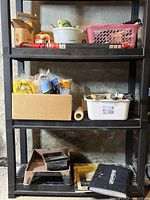 Photo of assorted painting supplies on black plastic shelving, containers with paint rollers, tape, and other supplies.