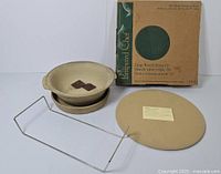 Full set of all included Pampered Chef stoneware items shown together: large pizza stone, baking bowl with base, metal frame stand, and original box.