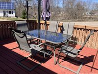 Full view of table with glass top, five chairs and umbrella on deck