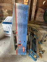 Photo showing large manual tile cutter box and assembled Mastercraft metal mitre box with blue arms and clamps.