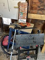 Photo of the Jobmate blue folding work bench with Mastercraft portable work bench beneath holding orange extension cord, metal miter box, and crowbar, plus red shop vacuum on floor.