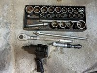 Full view of black air impact wrench, silver air ratchet, and tray filled with large sockets and extensions.