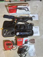 Overview photo showing all tools including Jobmate reciprocating saw in box, Mastercraft multi tool kit in black case, Jobmate detail sander with box and sanding sheets, and Power jigsaw on concrete floor.