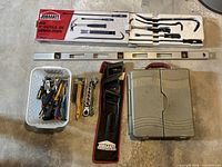 Full view of assorted hand tools including hand tools in basket, pry bars in black fabric case, demolition saws in white box, metal level, and Crescent ratchet set closed plastic case.