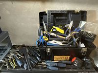 Full view of toolbox opened with many hand tools inside and around it including pliers, screwdrivers, ruler, scissors, measuring tape, and a ratchet set.