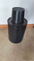 Stack of black plastic net pots with perforated sides and wide rim, approximately 10 inches in size.