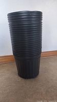 Stack of 22 new black plastic soft pots, cylindrical with ribbed sides, showing size and material.