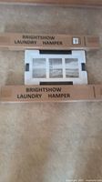Two Brightshow laundry hampers in cardboard boxes and a framed picture of the Golden Gate Bridge in black and white packed with styrofoam.