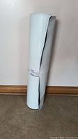 Tall roll of white poly with a visible black edge, standing upright on a floor against a white wall.