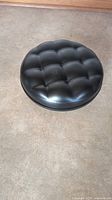 Top view of the black tufted padded round seat of the stool