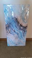 Full view of the rectangular blue abstract art piece standing vertically, covered in protective plastic.