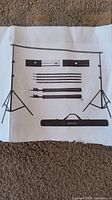 Printed instruction/manual sheet showing contents and assembly of backdrop stand kit with stands, rods, clamps, and carry bag.