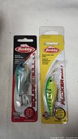 Front view of two sealed Berkley fishing lures in factory packaging: the Squirrel 5.5 and Flicker Shad 7 models.