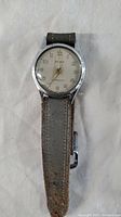 Top view of silver-tone vintage wristwatch with white dial and worn gray fabric strap.