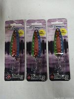 Photo showing three sealed Len Thompson Dimpled Series metal fishing lures with multicolor gradient and treble hooks attached.