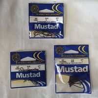 Three packs of Mustad hooks sealed in factory packaging on a white surface