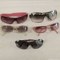Top-down view of all five pairs of sunglasses arranged side by side on a cloth surface showing different frame styles and colors.