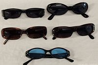 Five sunglasses in varying styles and colors laid out on a fabric surface.