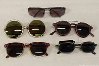 Top down view of 5 pairs of sunglasses laid flat on white surface, showing various frame styles and lens colors.