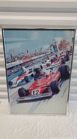 Framed vintage F1 racecar poster showing a red car #12 and blue car #28 on the race track with crowds in the background.