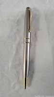 Closed ballpoint pen showing silver-tone body with gold-tone clip and tip.