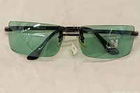 Front view of rimless green lens sunglasses with black arms and nose pads. Shows 100% UV protection sticker and Nygard branding on lens.