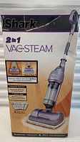 Front of box showing Shark 2-in-1 Vac Then Steam upright floor cleaner with vacuum and steam mop functions including product image and feature highlights.