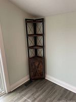Full view of a corner shelf placed in a corner against two walls, showing metal frame, wooden shelves and cabinet door at the bottom