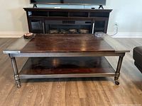 Full view of rectangular coffee table with wood top and metal detailing on a hardwood floor, showing tabletop, legs on wheels, and lower shelf.