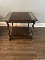 Front view of square end table with wood top and bottom shelf accented with metal trim and legs.