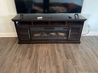 Dark wood fireplace TV stand with electric fireplace insert, two glass door cabinets, and three open shelves, with a flat-screen TV on top.