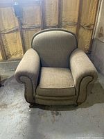 Front view of the upholstered arm chair showing the rolled arms, nailhead trim, cushioned seat, and overall condition needing cleaning.