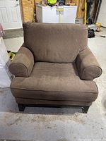 Front view of a single large brown upholstered armchair with cushioned seat, back, and armrests. Slight signs of use visible on fabric.