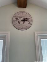 Photo of a round wall clock featuring a world map print, black hands, and minimal hour markers, mounted on a wall beneath a wooden ceiling beam.