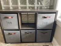 Front view of wooden cube shelf unit with five gray fabric bins and one empty compartment.