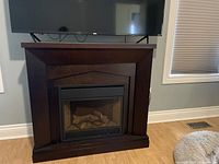 Electric fireplace with dark wood mantel located in a living room, showing the front and surroundings including TV above and windows.