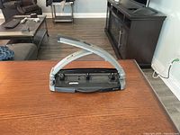 Photo of a silver metal heavy duty 3-hole punch placed on a table in a living room environment