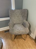 Photo of a modern decorative sofa chair with gray fabric and wooden legs placed in a corner.