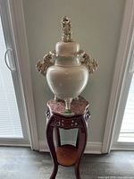Front view of the large antique ceramic urn with dragon finial and handles on a carved wooden stand