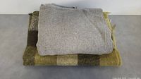 Two folded wool blankets: grey on top and green checkered underneath.