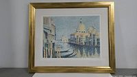 Framed color lithograph of Venice scene showing gondolas, buildings, and domed structure with golden frame on white background.