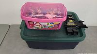 Pink LEGO storage box filled with assorted LEGO bricks and pieces, positioned alongside a LEGO Batman clock figure.