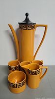 Full set of orange and black Greek Key design pottery coffee pot, three small cups, creamer, and sugar container