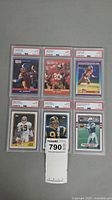 Six PSA graded NFL football cards displayed in two rows of three. Cards have red/white PSA labels with grades mostly 8 and one 9. Includes John Elway, Jerry Rice, Bernie Kosar cards.